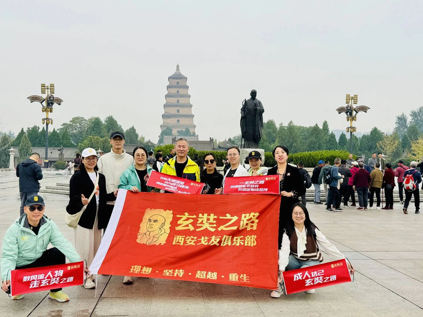 塔与人物雕像前的团队合影,横幅写有玄奘之路西安戈友俱乐部